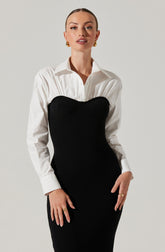 A woman is wearing a classic white button-up shirt with long sleeves, tucked into a black, form-fitting, ribbed knit dress with a sweetheart neckline over the bust. She is accessorized with gold hoop earrings and gold rings on her fingers.